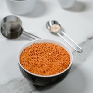 Red lentils in a bowl on marble, surrounded by measuring spoons.