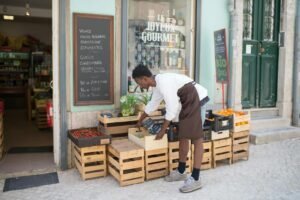 A worker arranges fruit crates outside a grocery store in Portugal, adding vibrant oranges and strawberries.